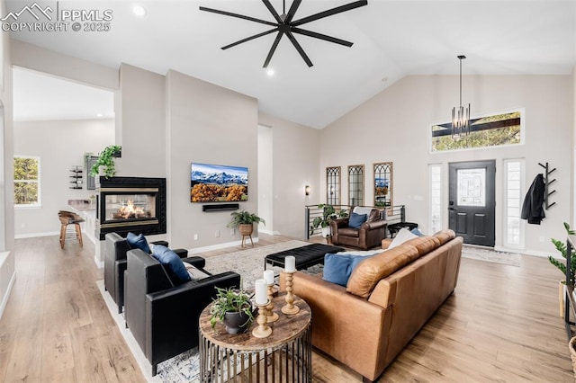 living room featuring a multi sided fireplace, light hardwood / wood-style flooring, high vaulted ceiling, and ceiling fan with notable chandelier