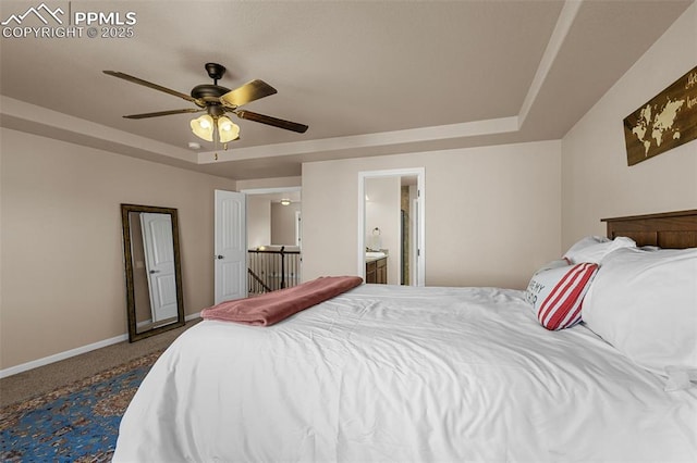 carpeted bedroom with a tray ceiling, ensuite bath, and ceiling fan