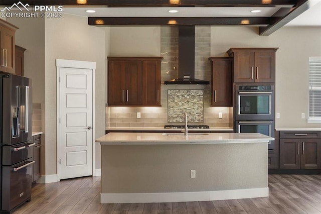 kitchen with hardwood / wood-style flooring, an island with sink, wall chimney range hood, and appliances with stainless steel finishes