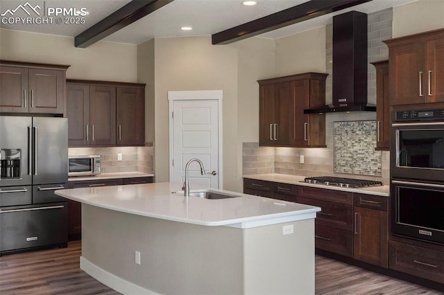 kitchen with a kitchen island with sink, wall chimney range hood, sink, beamed ceiling, and stainless steel appliances