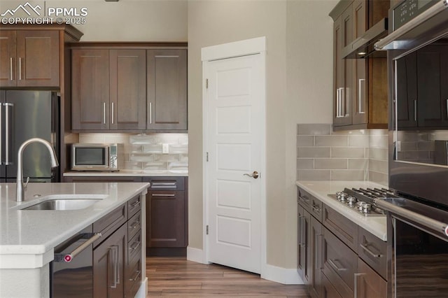 kitchen featuring appliances with stainless steel finishes, backsplash, light stone counters, sink, and light hardwood / wood-style floors