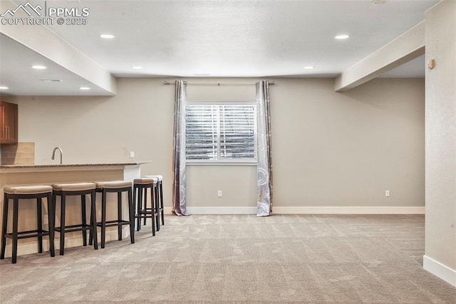 kitchen with light stone countertops, sink, kitchen peninsula, light colored carpet, and a breakfast bar