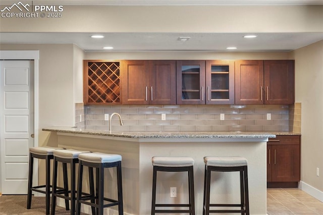 kitchen featuring a breakfast bar, sink, light stone countertops, tasteful backsplash, and kitchen peninsula