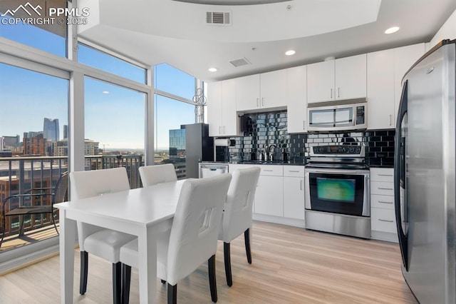 kitchen featuring tasteful backsplash, white cabinetry, light hardwood / wood-style flooring, and appliances with stainless steel finishes