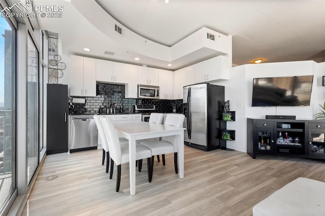 kitchen with decorative backsplash, stainless steel appliances, light hardwood / wood-style floors, white cabinetry, and plenty of natural light