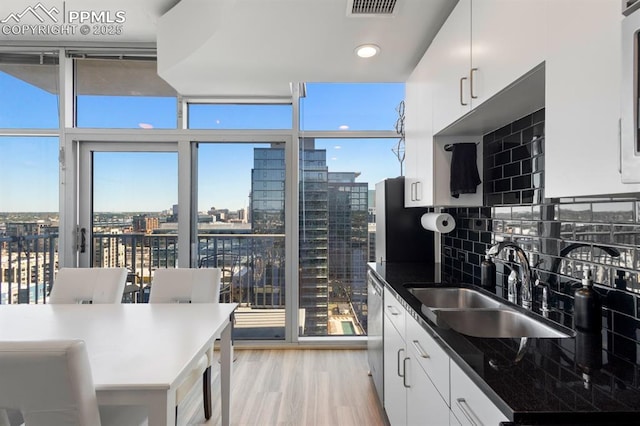 kitchen featuring backsplash, expansive windows, sink, light hardwood / wood-style flooring, and white cabinetry