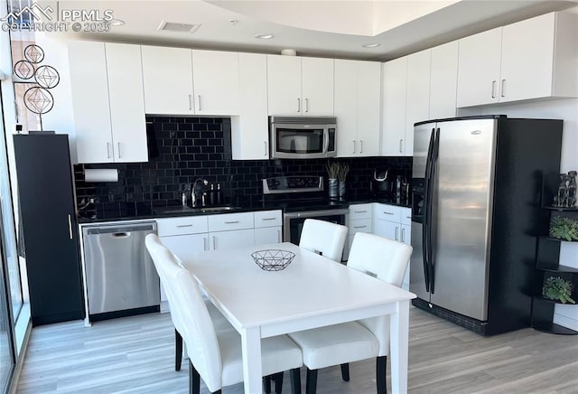 kitchen featuring appliances with stainless steel finishes, light wood-type flooring, tasteful backsplash, sink, and white cabinets