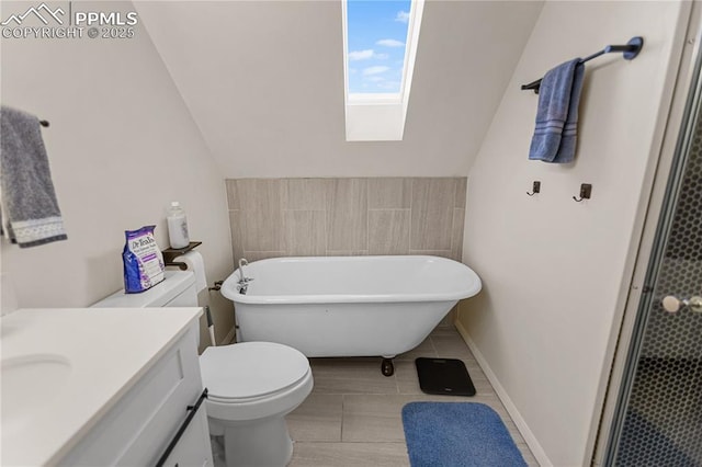 bathroom featuring a washtub, tile patterned flooring, lofted ceiling with skylight, toilet, and vanity