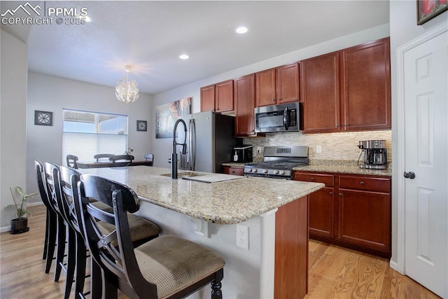 kitchen with a kitchen bar, an island with sink, light hardwood / wood-style floors, and appliances with stainless steel finishes