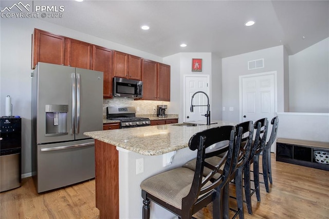 kitchen featuring sink, stainless steel appliances, light hardwood / wood-style flooring, a kitchen island with sink, and a breakfast bar