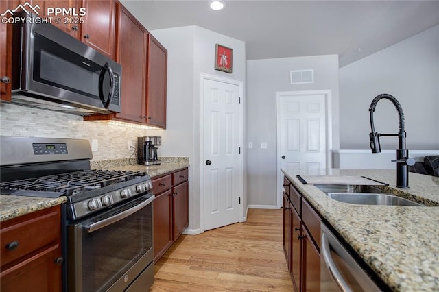 kitchen featuring light stone countertops, sink, tasteful backsplash, light hardwood / wood-style floors, and appliances with stainless steel finishes