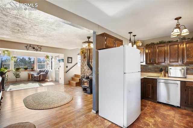 kitchen featuring white refrigerator, decorative light fixtures, a wood stove, stainless steel dishwasher, and decorative backsplash