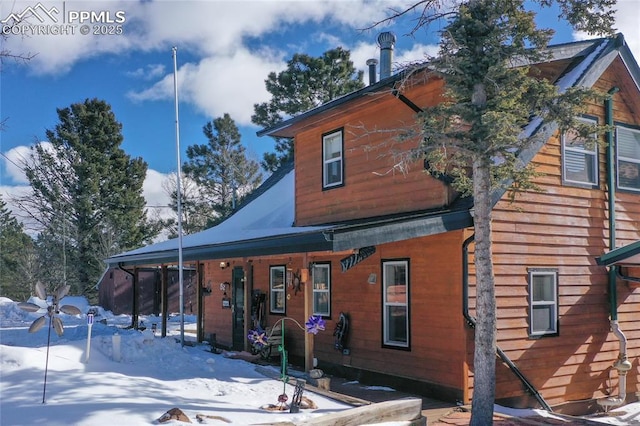 snow covered rear of property featuring covered porch