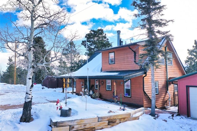 snow covered back of property featuring a porch and a garage