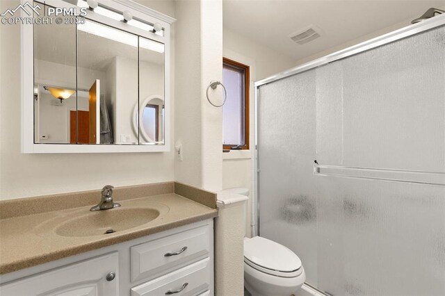 bathroom featuring vanity, toilet, and a shower with shower door