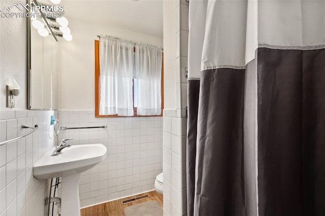 bathroom with sink, walk in shower, wood-type flooring, toilet, and tile walls