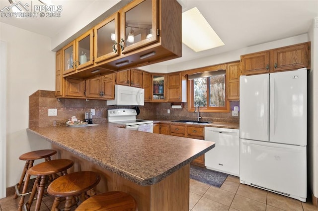 kitchen featuring backsplash, kitchen peninsula, white appliances, and sink