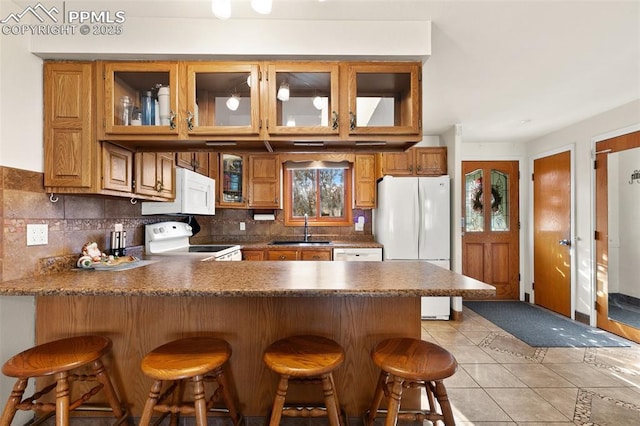 kitchen featuring sink, backsplash, kitchen peninsula, white appliances, and a breakfast bar area