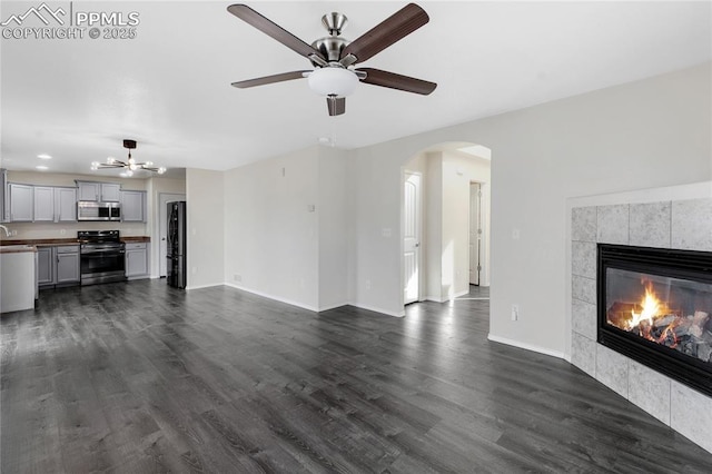 unfurnished living room with a tile fireplace, dark hardwood / wood-style flooring, and ceiling fan with notable chandelier