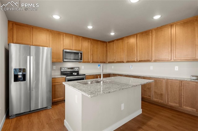 kitchen featuring a center island with sink, sink, light wood-type flooring, light stone countertops, and stainless steel appliances