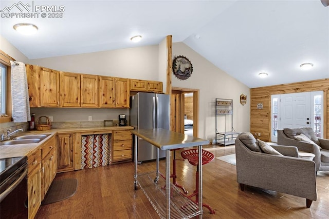 kitchen featuring sink, high vaulted ceiling, dark hardwood / wood-style floors, stainless steel fridge, and wood walls