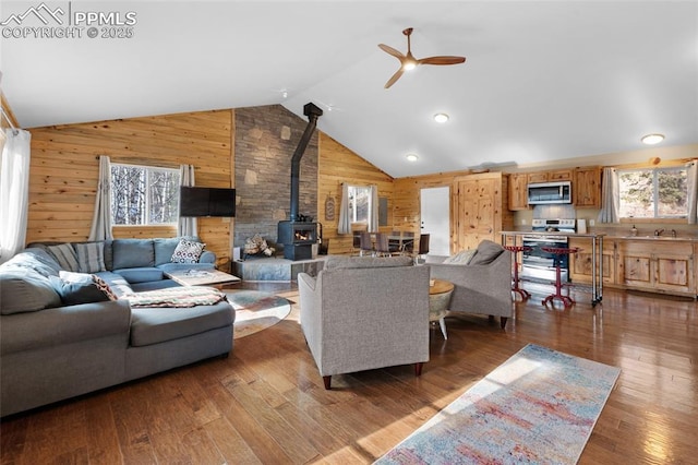 living room featuring wood walls, a wood stove, dark wood-type flooring, vaulted ceiling, and ceiling fan