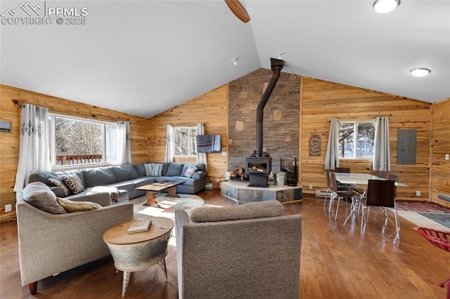 living room featuring a wood stove, plenty of natural light, vaulted ceiling, and electric panel