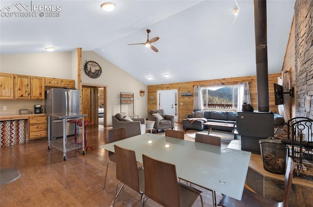 dining room featuring ceiling fan, hardwood / wood-style flooring, a wood stove, lofted ceiling, and wood walls