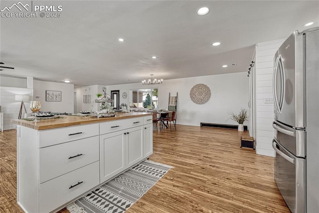 kitchen featuring light hardwood / wood-style flooring, stainless steel fridge, butcher block countertops, a kitchen island, and white cabinetry