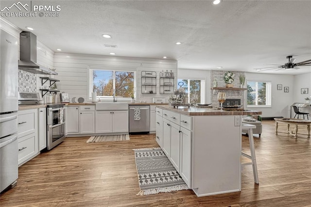 kitchen with white cabinets, a breakfast bar area, wall chimney exhaust hood, a textured ceiling, and stainless steel appliances