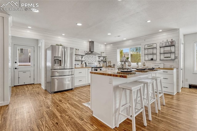 kitchen with a breakfast bar, a center island, white cabinets, wall chimney exhaust hood, and stainless steel appliances