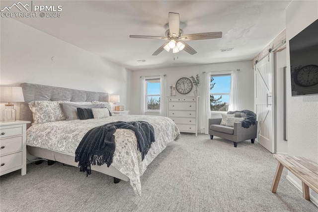 carpeted bedroom with a barn door and ceiling fan