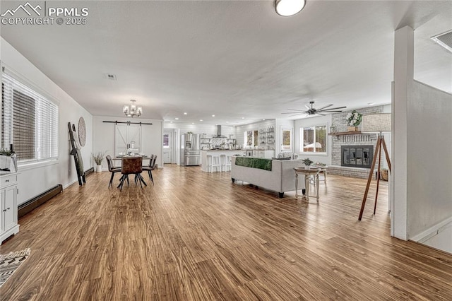 living room featuring a fireplace, ceiling fan with notable chandelier, a baseboard radiator, and hardwood / wood-style flooring