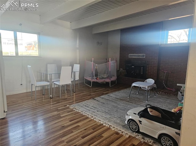 living area with hardwood / wood-style flooring, a brick fireplace, and beamed ceiling