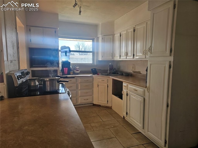 kitchen with stainless steel electric stove, rail lighting, sink, white cabinets, and light tile patterned floors