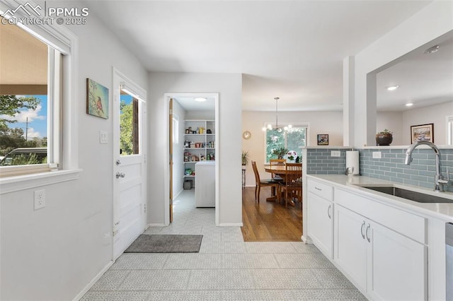 interior space featuring white cabinetry, sink, an inviting chandelier, pendant lighting, and decorative backsplash