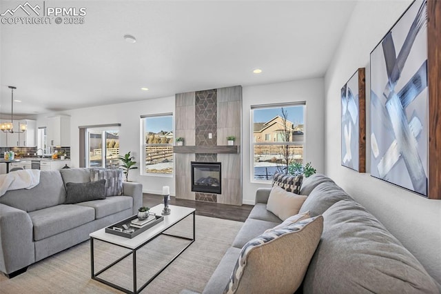 living room with a tiled fireplace, light wood-type flooring, sink, and a chandelier