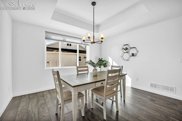 dining space with dark hardwood / wood-style floors, an inviting chandelier, and a tray ceiling