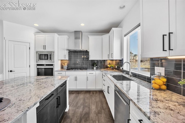 kitchen featuring wall chimney range hood, sink, appliances with stainless steel finishes, white cabinetry, and light stone counters