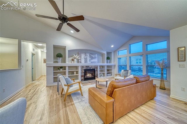 living room with built in shelves, ceiling fan, a stone fireplace, light hardwood / wood-style floors, and vaulted ceiling