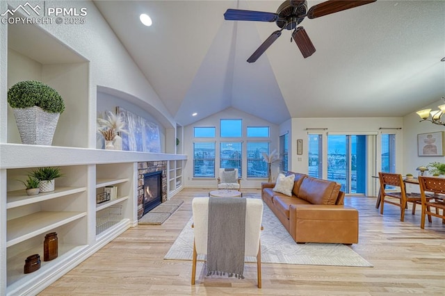 living room featuring built in shelves, a stone fireplace, lofted ceiling, ceiling fan with notable chandelier, and light wood-type flooring