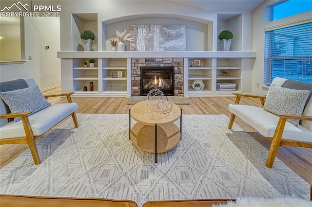 living area featuring a stone fireplace, built in features, and wood-type flooring