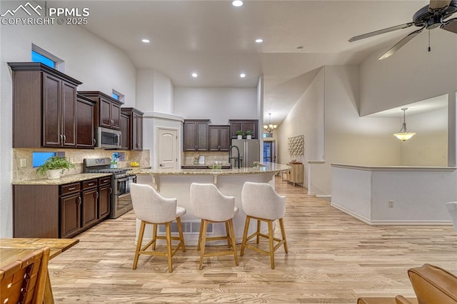 kitchen with a center island with sink, light stone countertops, stainless steel appliances, and a high ceiling