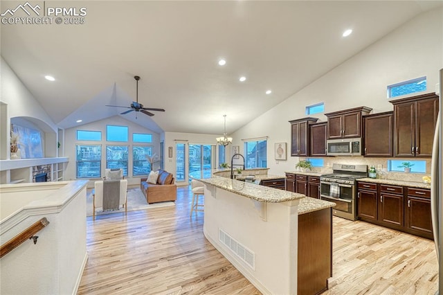 kitchen featuring appliances with stainless steel finishes, a breakfast bar, light hardwood / wood-style floors, hanging light fixtures, and an island with sink