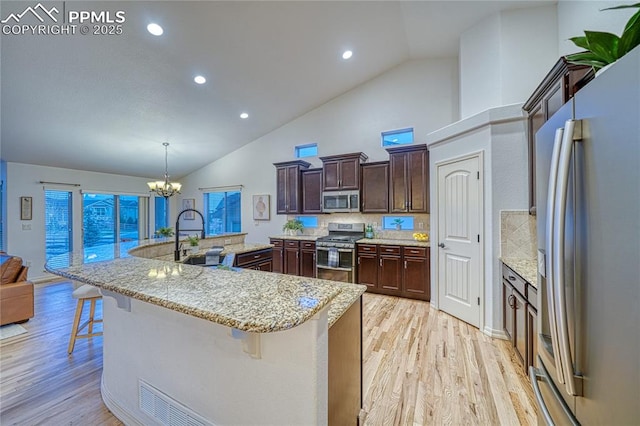 kitchen with light hardwood / wood-style flooring, decorative light fixtures, a kitchen bar, decorative backsplash, and appliances with stainless steel finishes