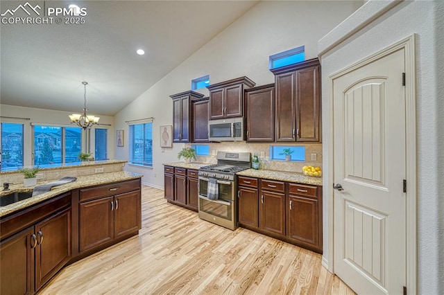 kitchen featuring dark brown cabinetry, hanging light fixtures, an inviting chandelier, vaulted ceiling, and appliances with stainless steel finishes