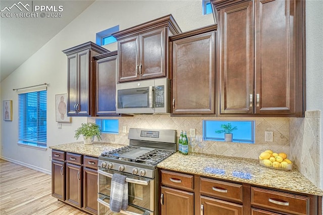 kitchen with decorative backsplash, appliances with stainless steel finishes, light stone counters, vaulted ceiling, and light hardwood / wood-style flooring