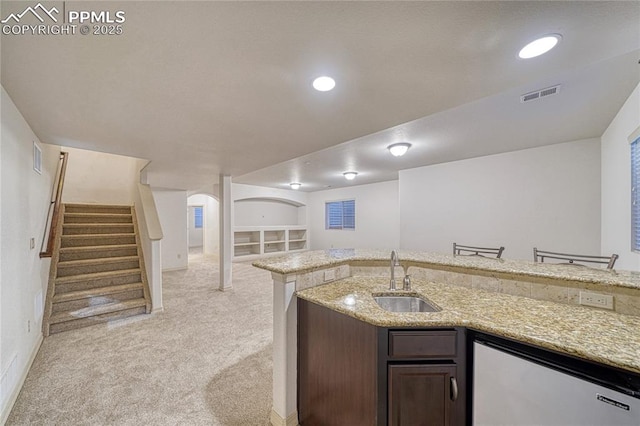 kitchen featuring light stone countertops, dark brown cabinets, built in shelves, sink, and dishwasher