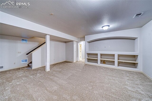 basement with built in features, light colored carpet, and a textured ceiling