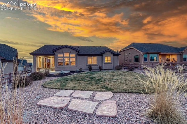 back house at dusk featuring a lawn and a patio area